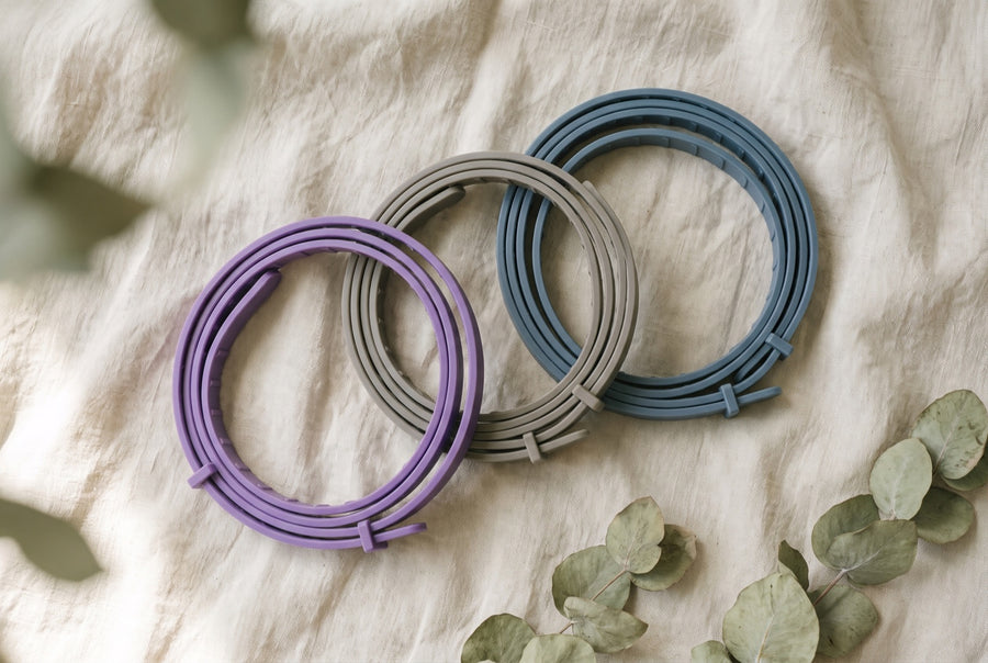 Three CollarZen collars coiled on linen in purple, grey and blue.
